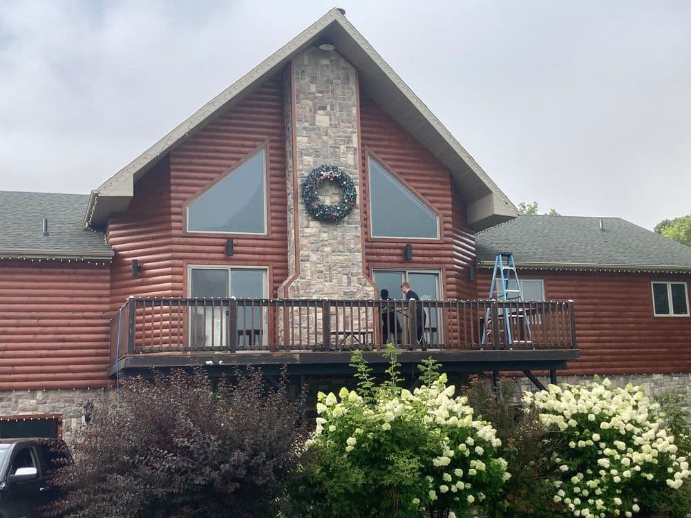 Log cabin house with stone accents, festive wreath, and a person working on the balcony.