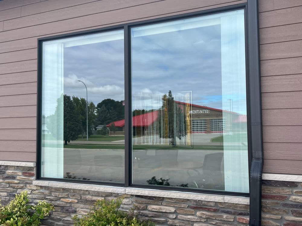 Modern window with reflection of a red building and cloudy sky, framed by stone and wood exterior.