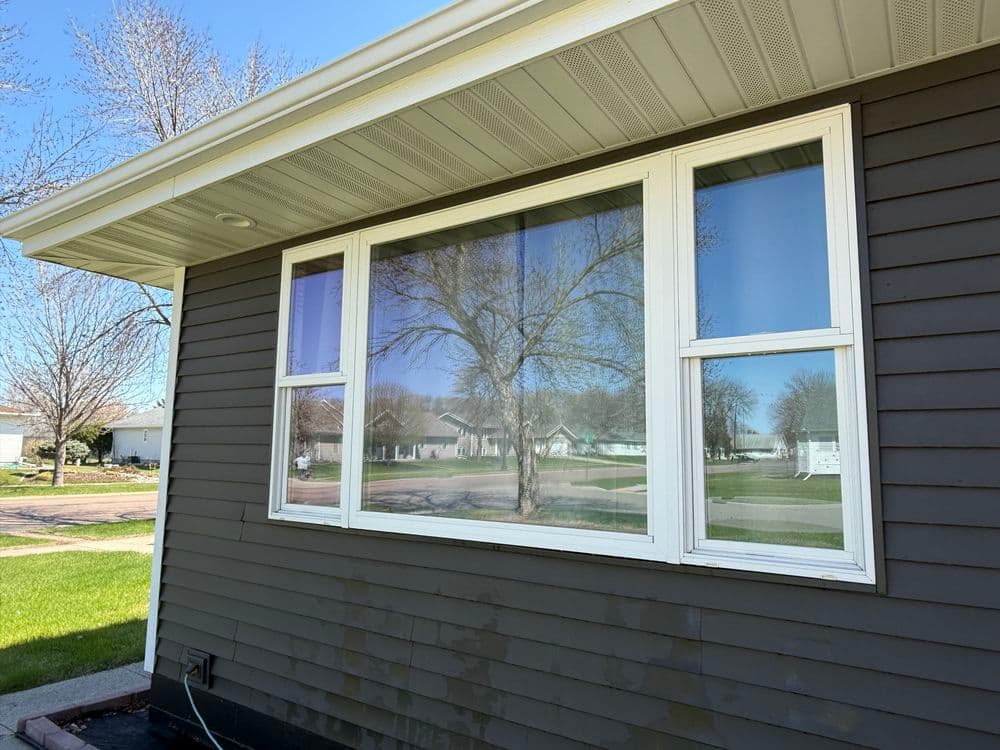 Modern window on a brown house exterior reflecting trees and blue sky.