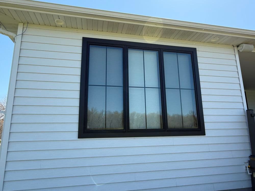 Black framed window with six panes on a white wooden house exterior. Clear blue sky above.