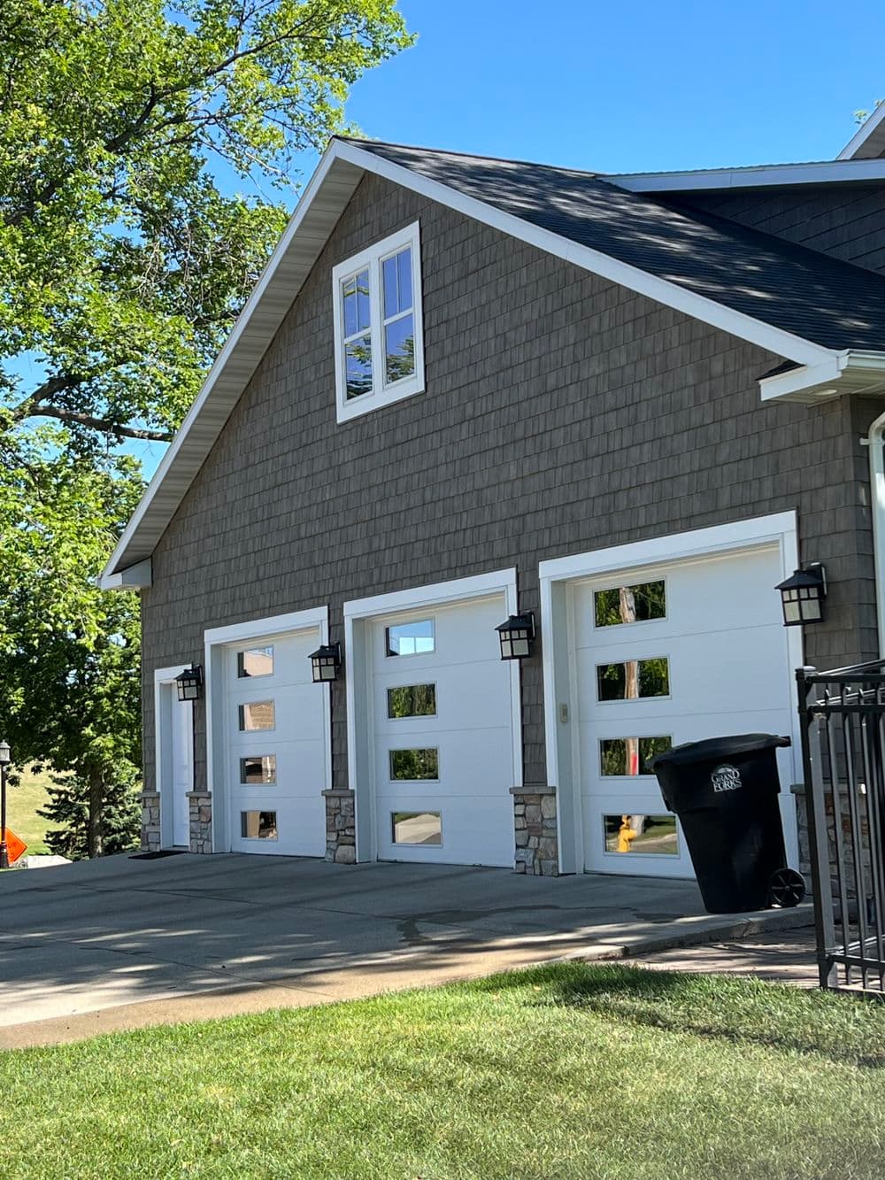 Modern home exterior with three garage doors, stone accents, and lush green landscaping.