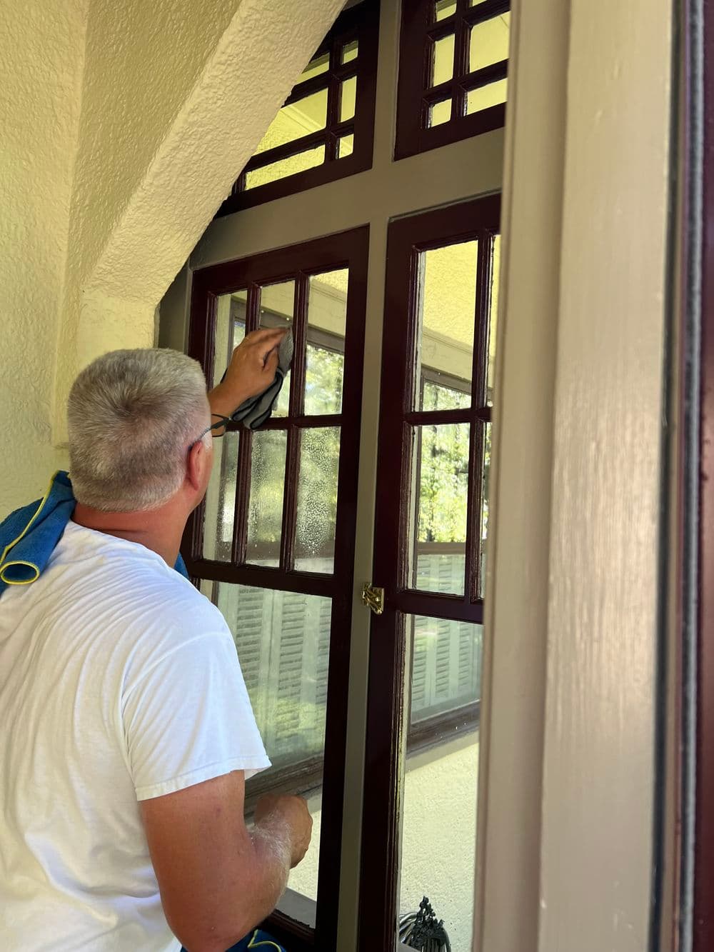 Man cleaning large, decorative windows with a cloth in a bright, airy room.