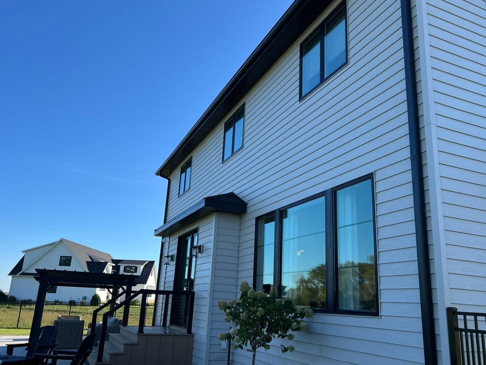 Modern two-story house with large windows and a deck under a clear blue sky.