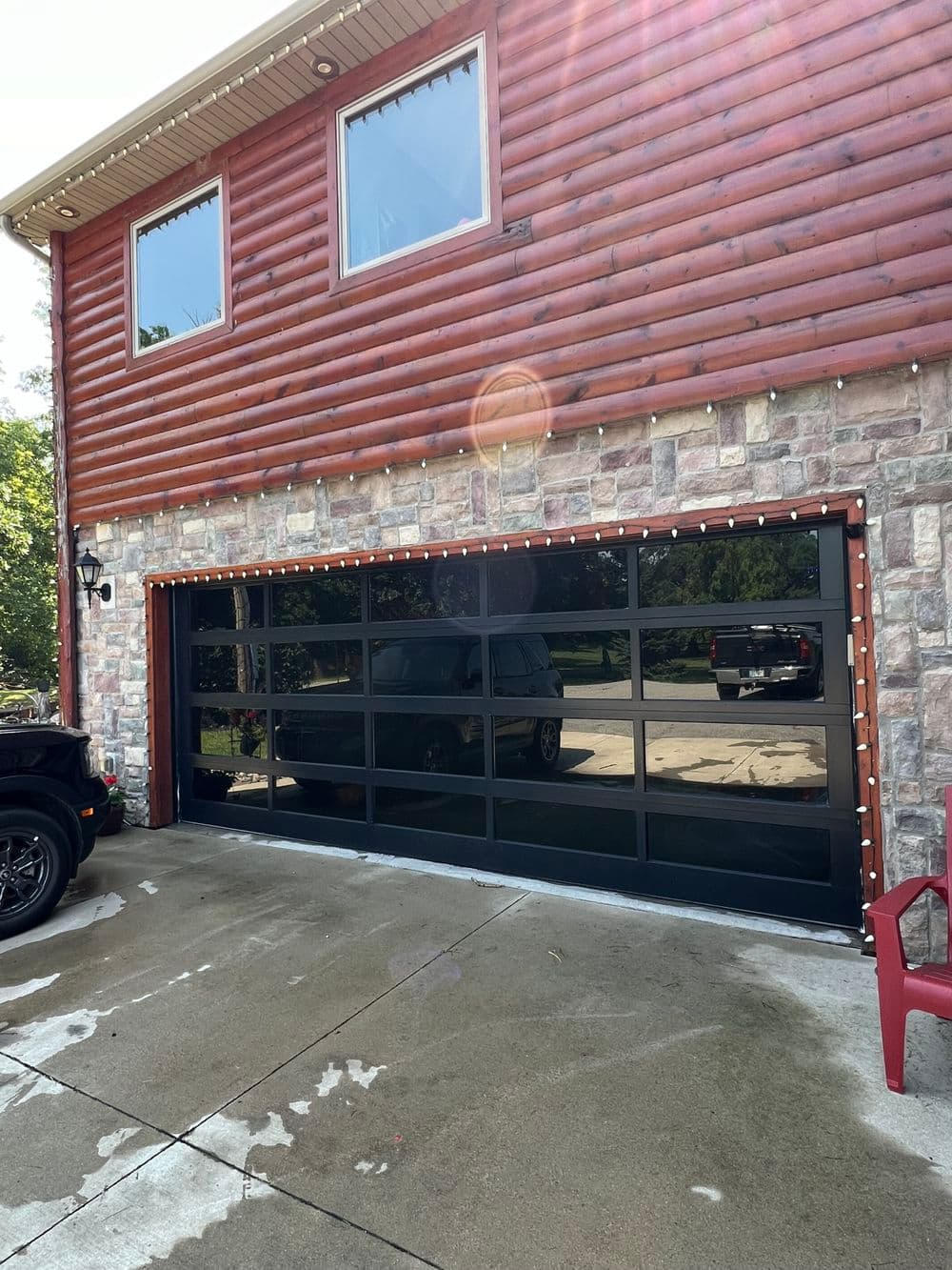 Modern black glass garage door on a log and stone house exterior.