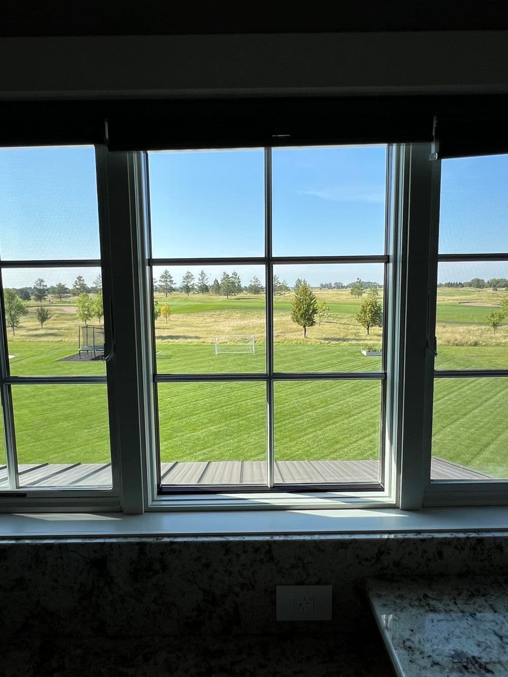 View from a window overlooking a lush green landscape and golf course. Clear blue sky.