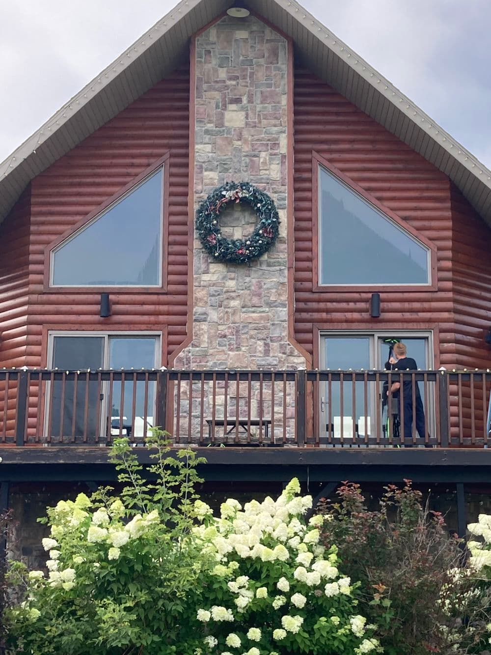 Wooden chalet with stone accents, large windows, and a floral foreground, enhancing its rustic charm.