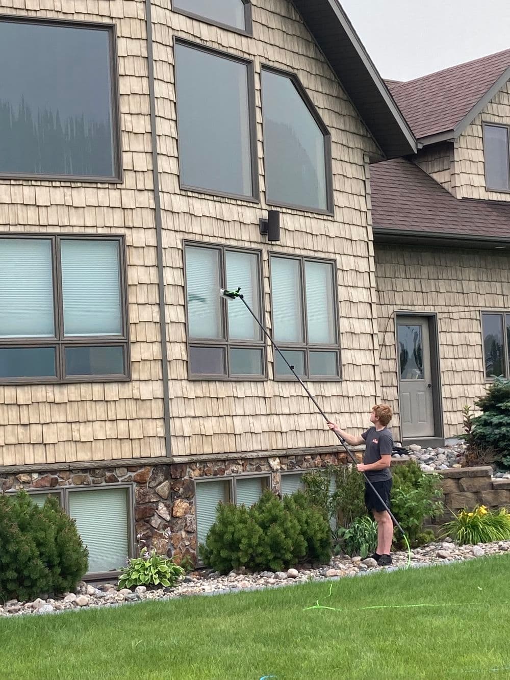 Person using a long pole to clean windows of a modern house with a stone exterior.