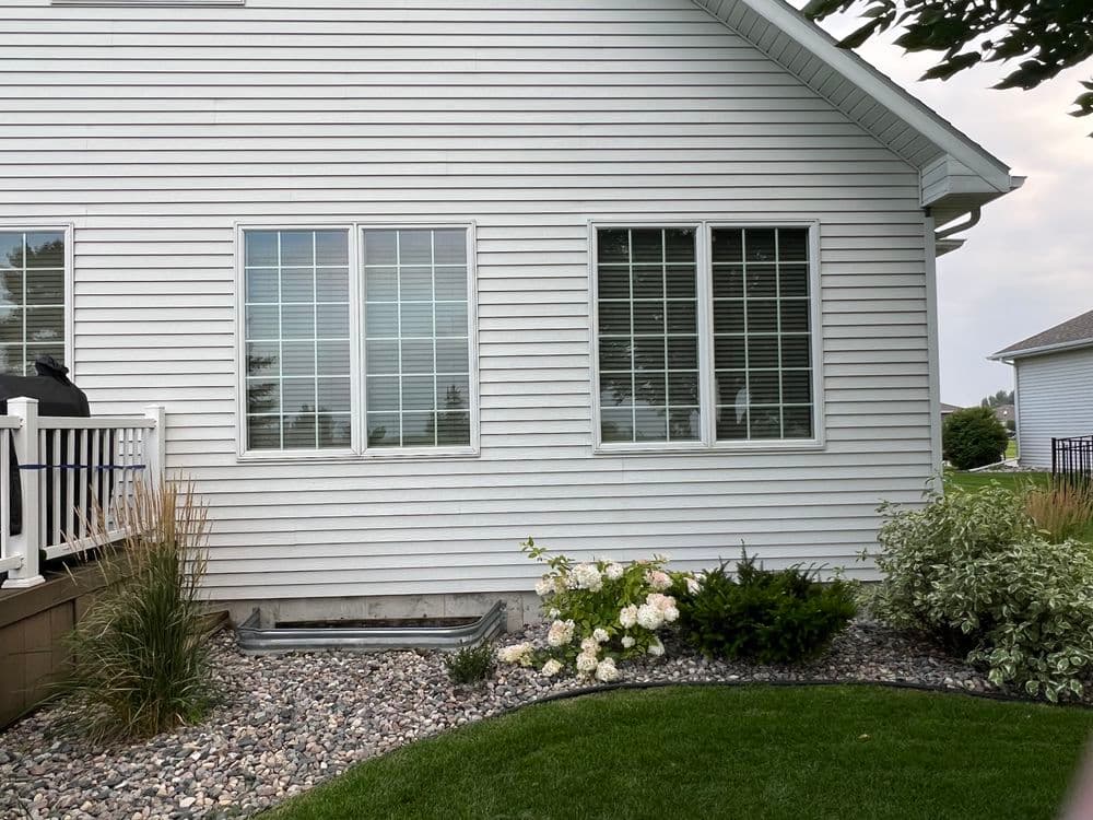 White house exterior featuring large windows, landscaped garden, and decorative stones.