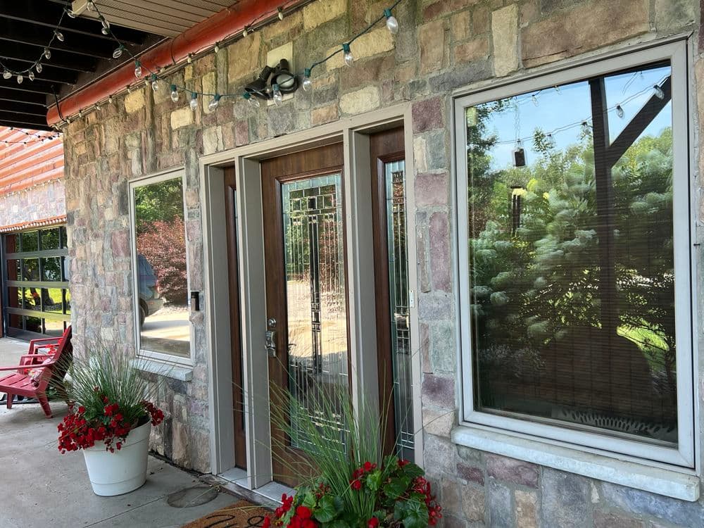 Charming stone exterior with wooden door, large windows, and vibrant red flower pots.