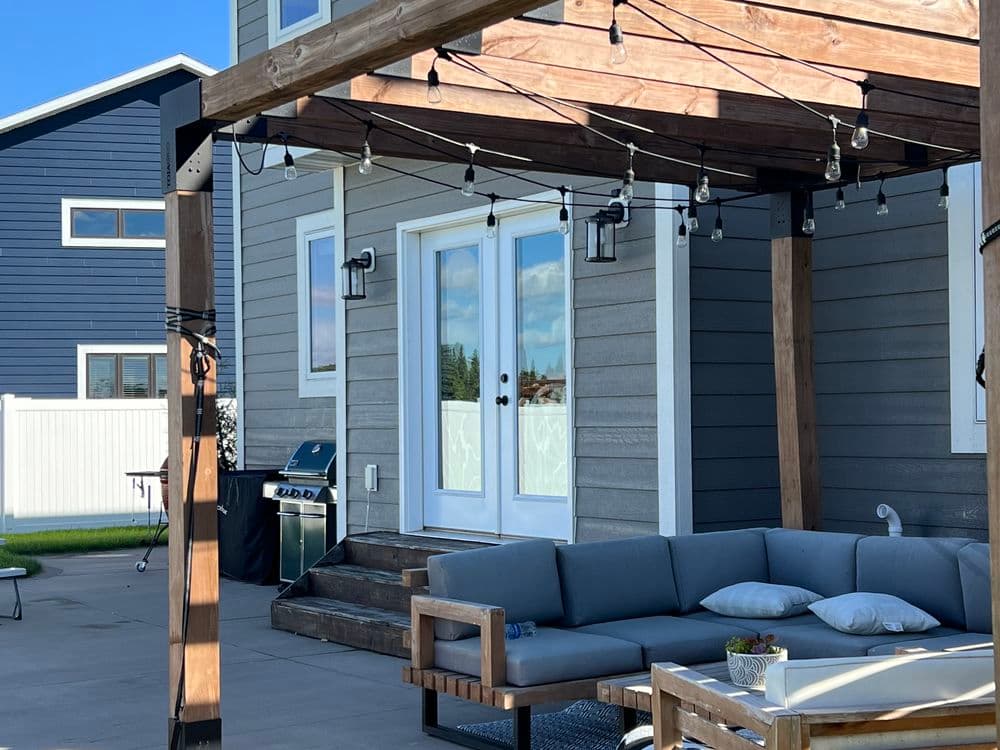 Modern outdoor patio with seating area, grill, and decorative string lights next to a house.