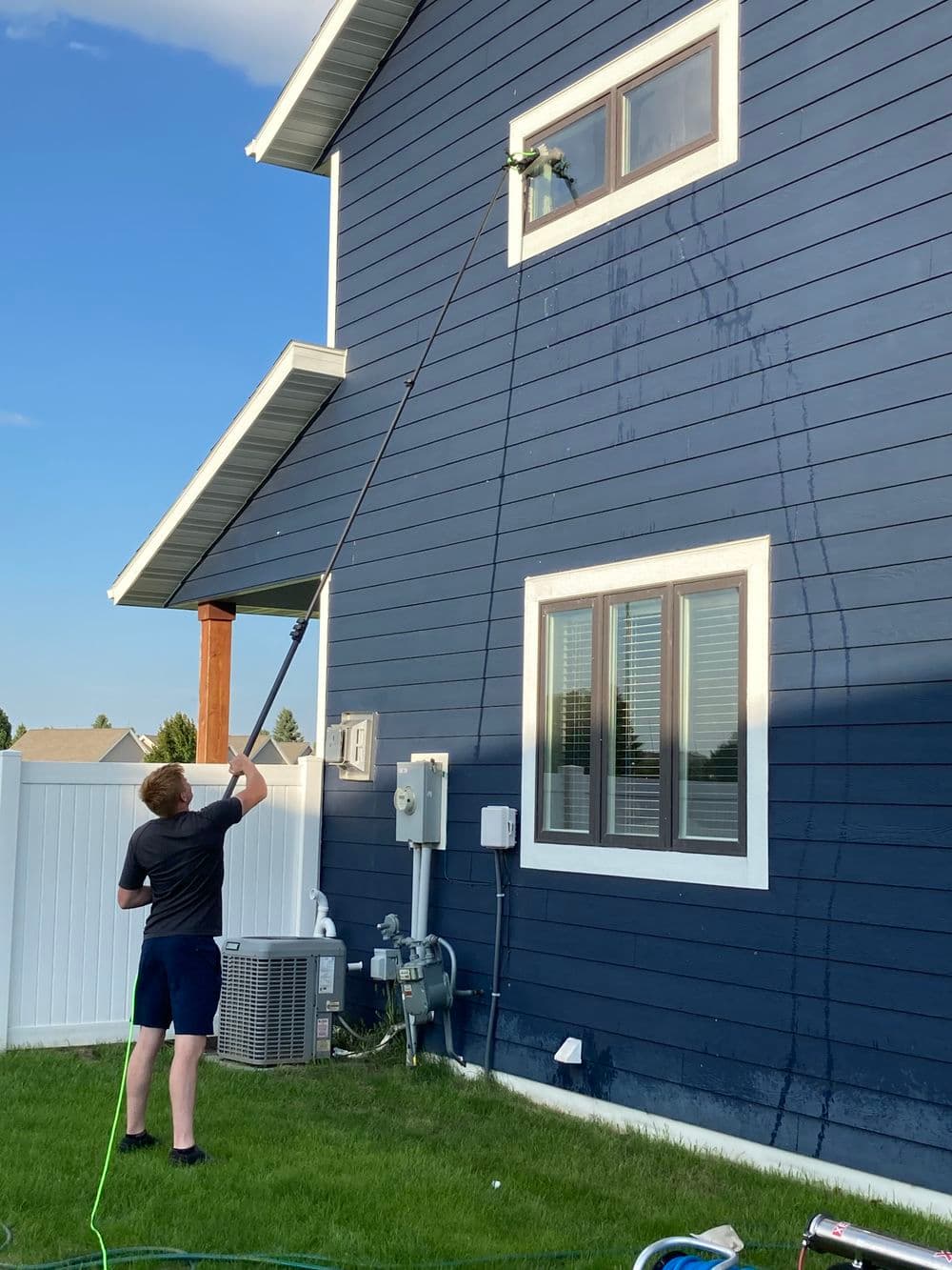 Person using a long reach tool to clean a window on a blue house exterior.
