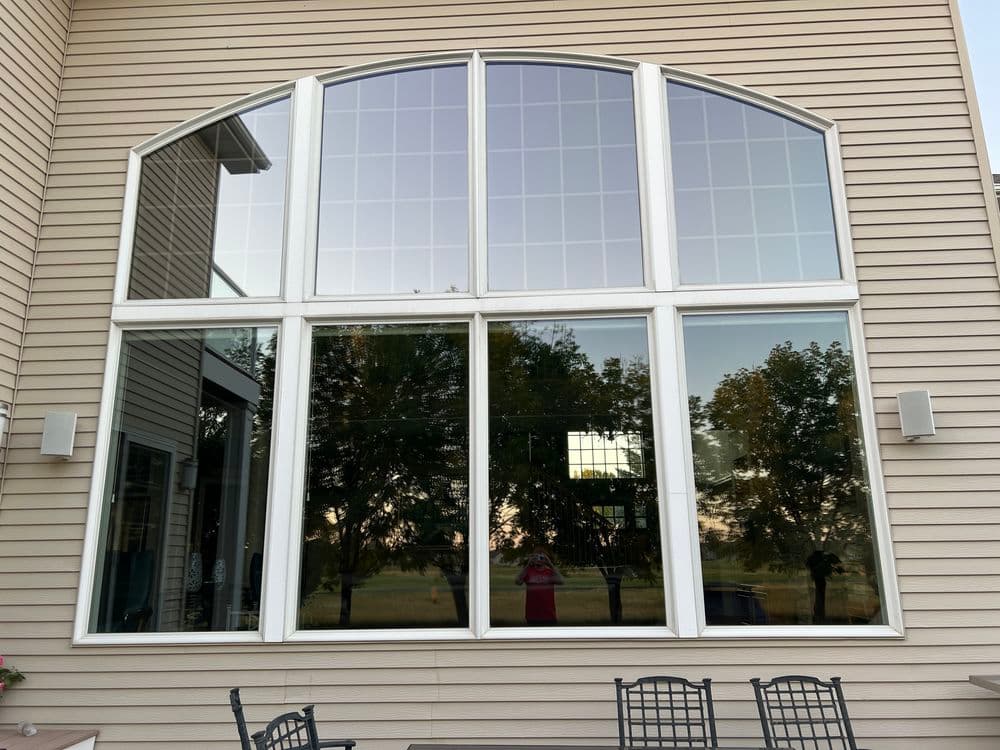 Large arched windows reflecting trees and a patio, enhancing outdoor views.