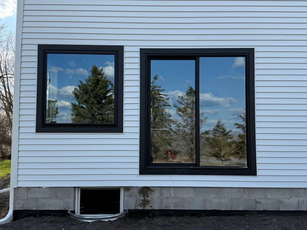 Modern home exterior featuring black framed windows and white siding with a scenic view.