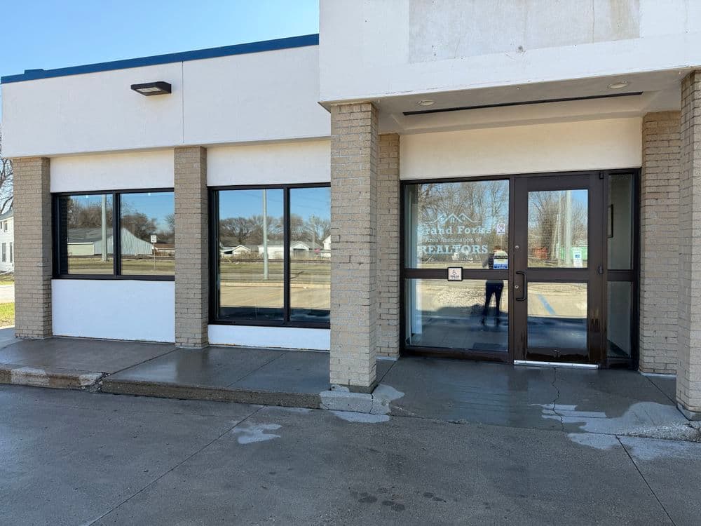 Entrance of Grand Fort Realtors office building with large windows and clean pavement.