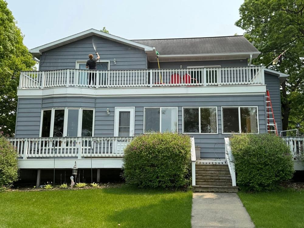 Person painting the exterior of a blue house with white railings and a green lawn.