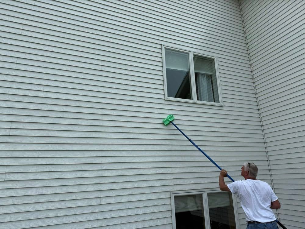 Person cleaning a house's vinyl siding with a long-handled brush.